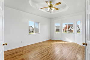 Empty room with light wood-type flooring, a raised ceiling, and a ceiling fan