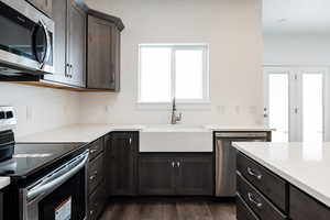 Kitchen with appliances with stainless steel finishes, dark wood-style floors, dark brown cabinets, and light stone counters
