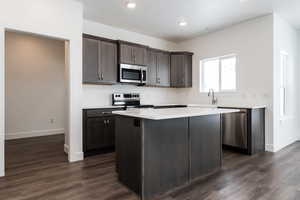 Photo of home built in past by OLO. Kitchen with appliances with stainless steel finishes, a kitchen island, dark wood finished floors, dark brown cabinets, and recessed lighting