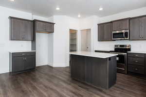 Photo of home built in past by OLO. Kitchen with stainless steel appliances, dark brown cabinetry, dark wood-type flooring, a kitchen island, and recessed lighting