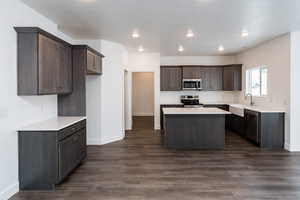 Photo of home built in past by OLO.  Kitchen featuring a center island, appliances with stainless steel finishes, dark brown cabinets, dark wood finished floors, and recessed lighting