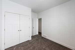 Unfurnished bedroom featuring dark colored carpet and a closet