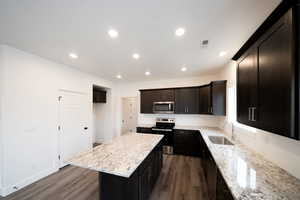 Photo of home built in past by OLO.  Kitchen featuring stainless steel appliances, light stone counters, recessed lighting, and dark wood-style flooring