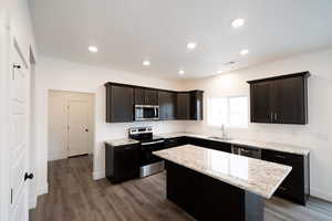 Photo of home built in past by OLO.  Kitchen with appliances with stainless steel finishes, a kitchen island, light stone countertops, dark brown cabinets, and dark wood-style flooring
