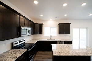 Photo of home built in past by OLO.  Kitchen with stainless steel appliances, light stone counters, dark brown cabinets, dark wood-style floors, and a kitchen island