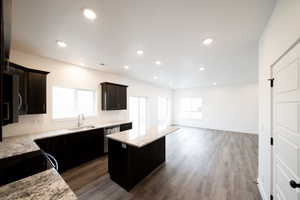 Photo of home built in past by OLO. Kitchen featuring light stone counters, a center island, dark wood-style flooring, dishwasher, and open floor plan