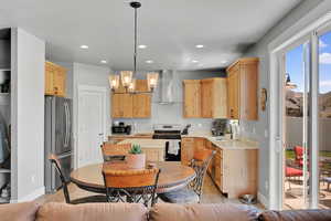 Kitchen with light brown cabinetry, stainless steel appliances, a chandelier, pendant lighting, and recessed lighting