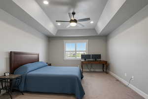 Bedroom featuring light carpet, a ceiling fan, a tray ceiling, recessed lighting, and an office area