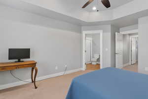 Bedroom with a ceiling fan, light carpet, connected bathroom, and a tray ceiling