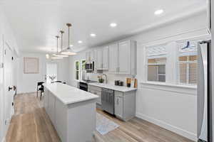 Kitchen with gray cabinets, a kitchen island, decorative light fixtures, light wood-style floors, and recessed lighting