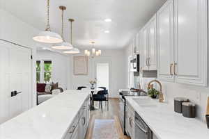 Kitchen featuring pendant lighting, light stone counters, stainless steel appliances, white cabinetry, and recessed lighting