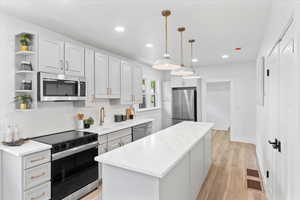 Kitchen featuring stainless steel appliances, hanging light fixtures, open shelves, white cabinets, and a center island
