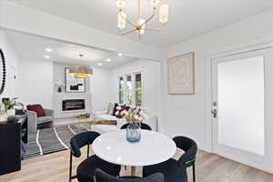 Dining room with light wood finished floors, a glass covered fireplace, recessed lighting, and a chandelier