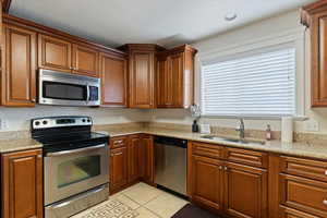 Kitchen featuring appliances with stainless steel finishes, light stone countertops, brown cabinetry, and recessed lighting