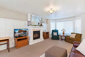 Living room featuring a glass covered fireplace, light colored carpet, and a decorative wall