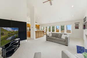 Living room with light carpet, a fireplace with flush hearth, high vaulted ceiling, recessed lighting, and ceiling fan