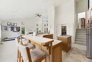 Kitchen featuring light countertops, freestanding refrigerator, a breakfast bar area, high vaulted ceiling, and brown cabinetry