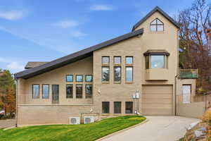 Side view of property exterior with a balcony, brick siding, driveway, a lawn, and an attached garage