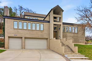 View of front of home featuring brick siding, a garage, driveway, stairway, and a chimney