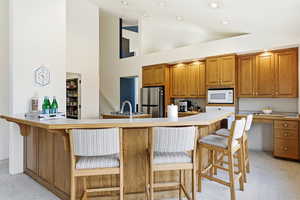 Kitchen featuring brown cabinetry, light colored carpet, a kitchen breakfast bar, and high vaulted ceiling
