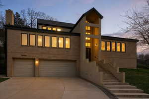 Modern home featuring stairway, an attached garage, concrete driveway, a chimney, and stucco siding