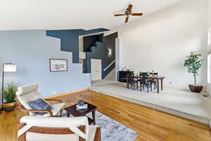 Living area with high vaulted ceiling, wood finished floors, stairs, and ceiling fan
