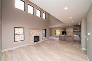 Unfurnished living room with a high ceiling, light wood-type flooring, a fireplace, and recessed lighting