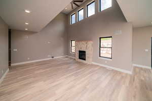 Unfurnished living room featuring recessed lighting, a glass covered fireplace, light wood-type flooring, a towering ceiling, and ceiling fan