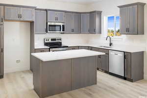 Kitchen with appliances with stainless steel finishes, a center island, light wood-style floors, and light stone counters
