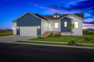 View of front of home with board and batten siding, a yard, driveway, roof with shingles, and a garage