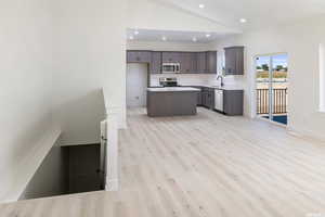 Kitchen featuring a center island, appliances with stainless steel finishes, recessed lighting, light wood-style floors, and lofted ceiling