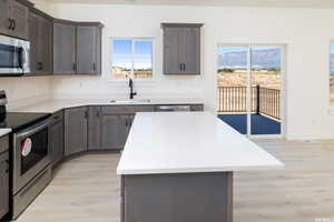 Kitchen featuring appliances with stainless steel finishes, light wood-style floors, a kitchen island, and light stone counters