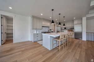 Kitchen featuring stainless steel appliances, a kitchen breakfast bar, pendant lighting, a center island with sink, and light wood-type flooring