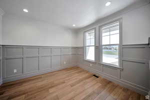 Unfurnished room featuring a decorative wall, wainscoting, light wood-style floors, recessed lighting, and ornamental molding