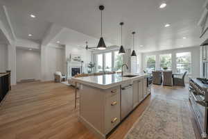 Kitchen with gray cabinets, open floor plan, pendant lighting, a glass covered fireplace, and a kitchen island with sink
