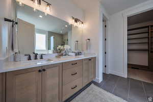 Primary bathroom with a shower stall, double vanity, dark tile patterned flooring, and a spacious closet