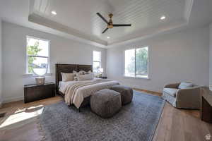 Primary bedroom with a tray ceiling, wooden ceiling, light wood finished floors, and ceiling fan