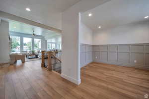 Hallway with an upstairs landing, a decorative wall, light wood finished floors, wainscoting, and recessed lighting