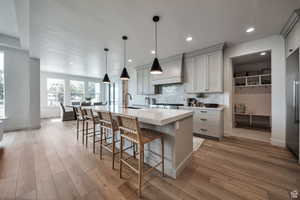 Kitchen with decorative backsplash, a breakfast bar, a kitchen island with sink, pendant lighting, and light wood finished floors
