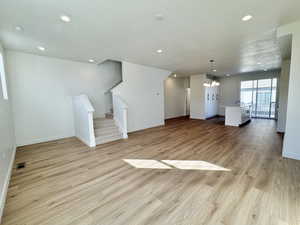 Unfurnished living room featuring a textured ceiling, stairway, a chandelier, light wood-style flooring, and recessed lighting