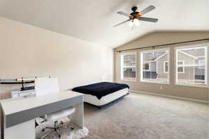 Carpeted bedroom featuring vaulted ceiling, ceiling fan, an office area, and a textured ceiling