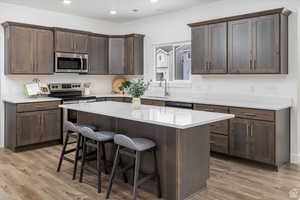 Kitchen with stainless steel appliances, a breakfast bar, dark brown cabinets, light wood-type flooring, and recessed lighting