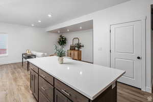 Kitchen with dark brown cabinets, a center island, light wood-style floors, recessed lighting, and light stone counters