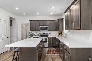 Kitchen featuring dark brown cabinetry, appliances with stainless steel finishes, dark wood finished floors, a kitchen island, and recessed lighting