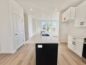Kitchen featuring white cabinets, a kitchen island with sink, stainless steel stove, light stone countertops, and recessed lighting