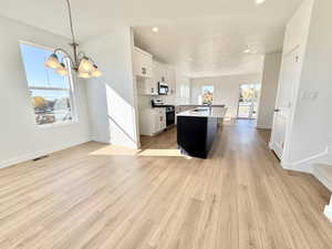 Kitchen featuring white cabinetry, appliances with stainless steel finishes, a center island with sink, open floor plan, and light wood-style floors