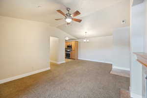 Unfurnished living room featuring light colored carpet, lofted ceiling, ceiling fan, a chandelier, and a fireplace