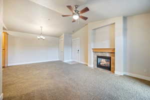 Unfurnished living room with lofted ceiling, light colored carpet, a tile fireplace, a chandelier, and a ceiling fan