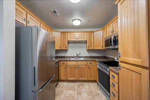 Kitchen featuring stainless steel appliances, dark countertops, a textured ceiling, light tile patterned floors, and brown cabinets