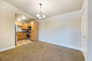 Kitchen with pendant lighting, light carpet, dark countertops, a chandelier, and lofted ceiling